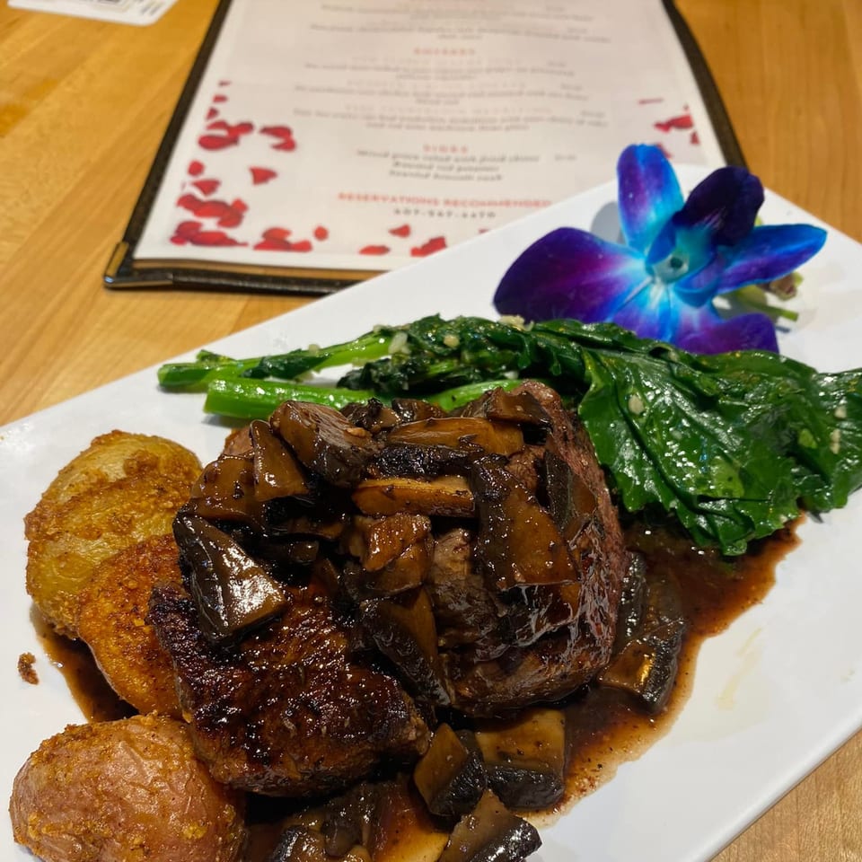 Braised short ribs with mushroom gravy, roasted potatoes, and greens, garnished with an orchid.