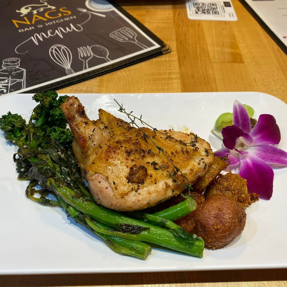 A plate of roasted chicken, broccolini, potatoes, and a purple orchid garnish at NAGS Bar and Kitchen.