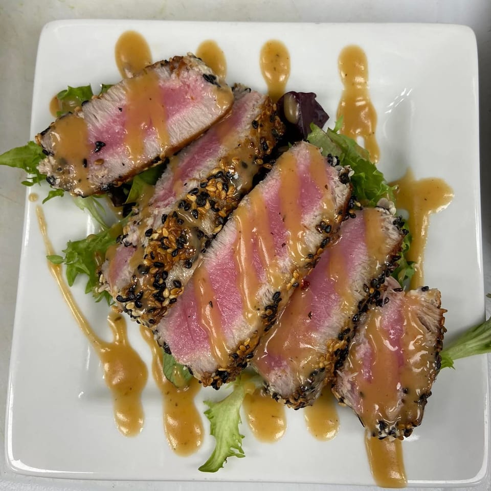 Seared tuna slices with sesame crust, drizzled with sauce, served on a bed of greens.