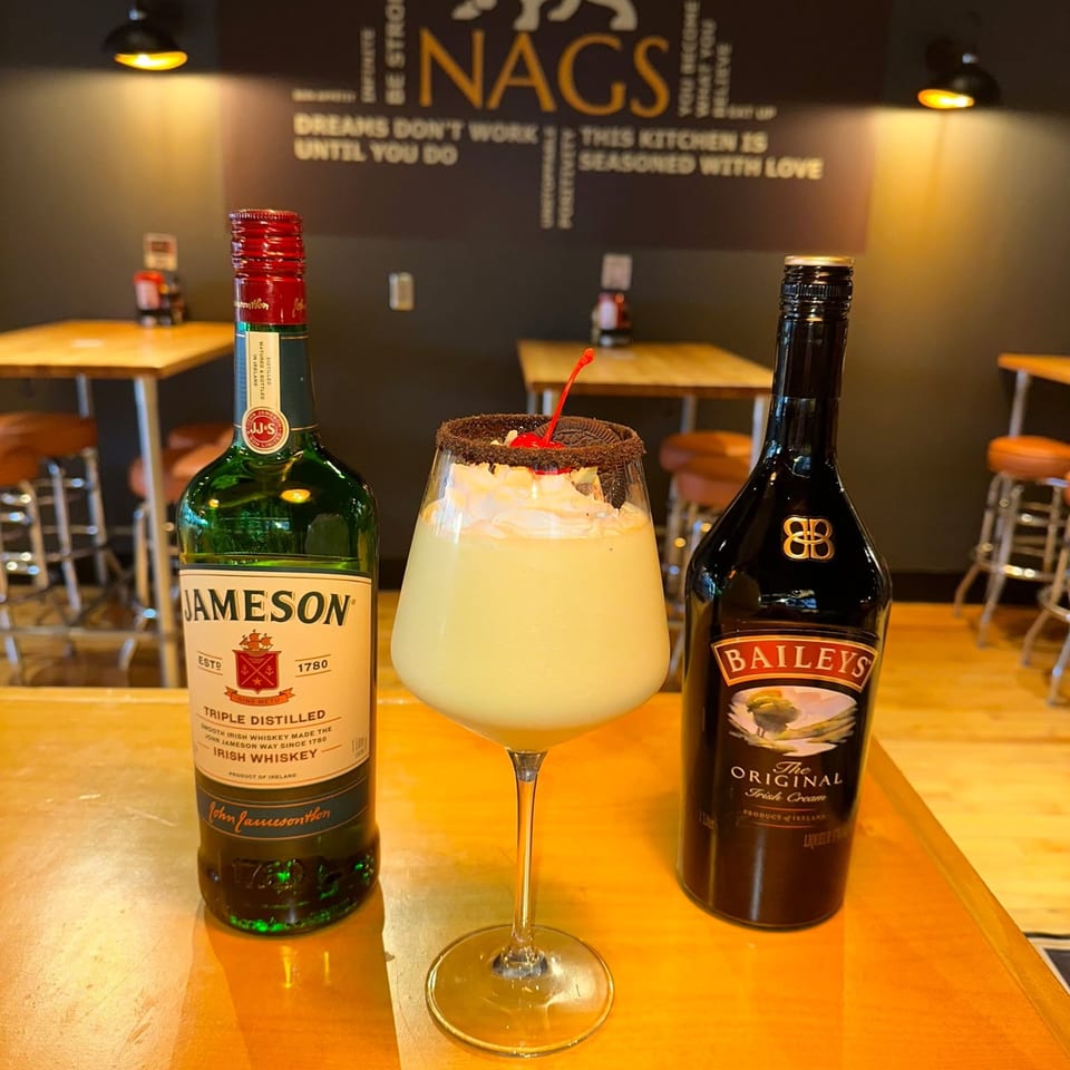A creamy cocktail with whipped cream, an Oreo, and a cherry, flanked by Jameson and Baileys bottles.
